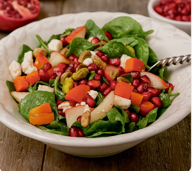 bright spinach salad with pears, pomegranate, and pistachios in white bowl