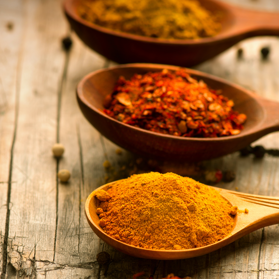 Four wooden spoons filled with different spices on a rustic wooden surface