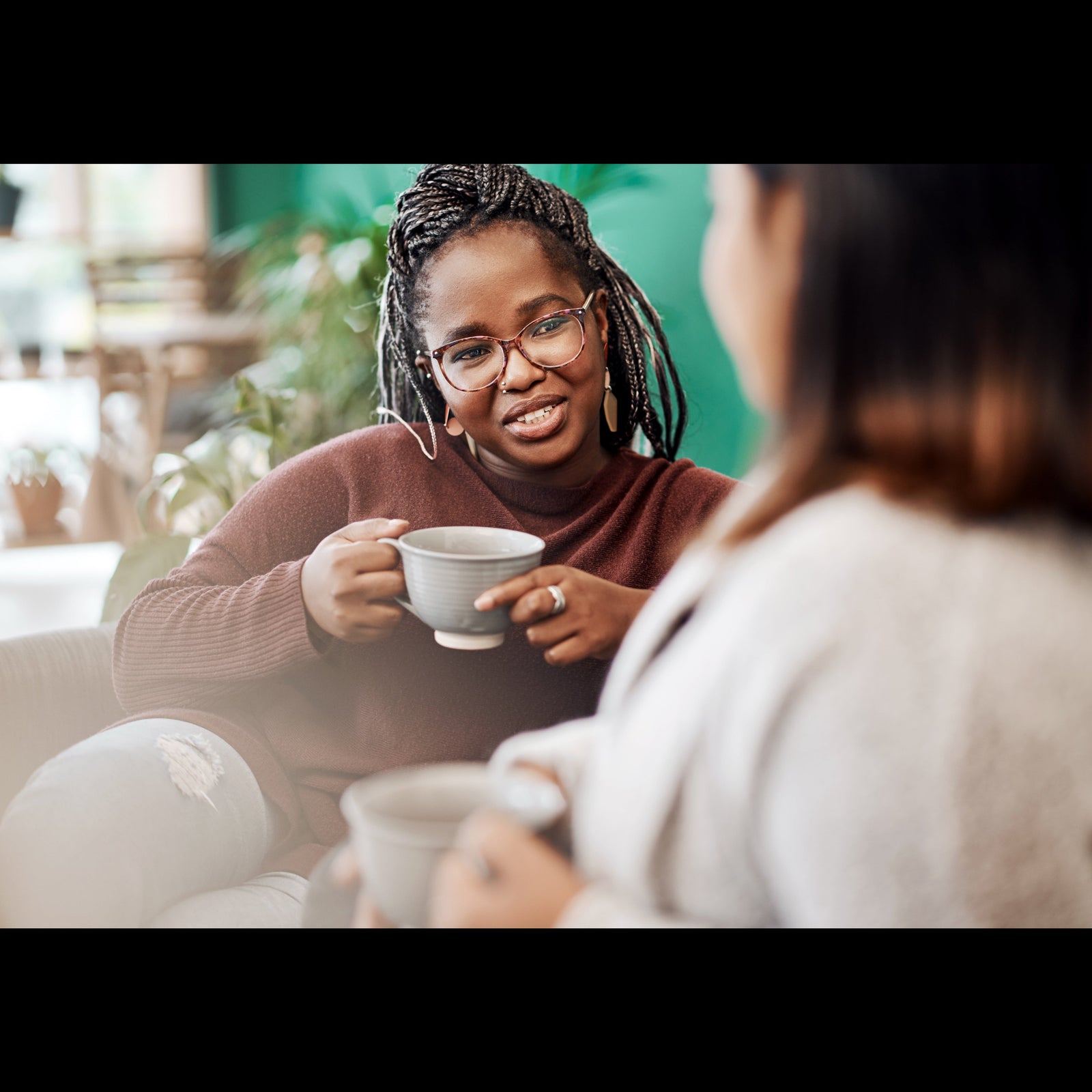 Two people sitting together, one holding a mug, in a casual indoor setting.