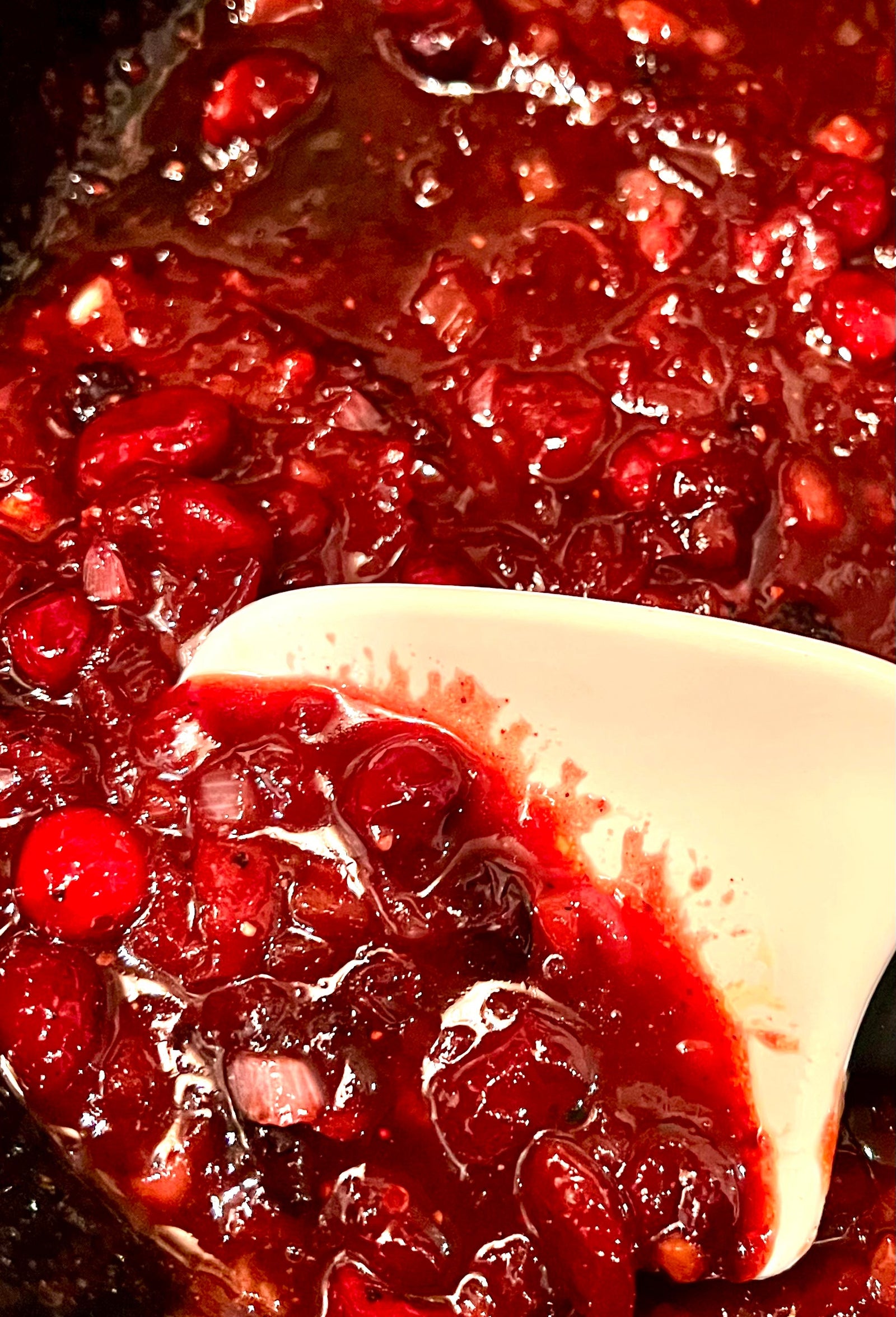 bright red cranberry simmering in a cast iron skillet with a white spoon.