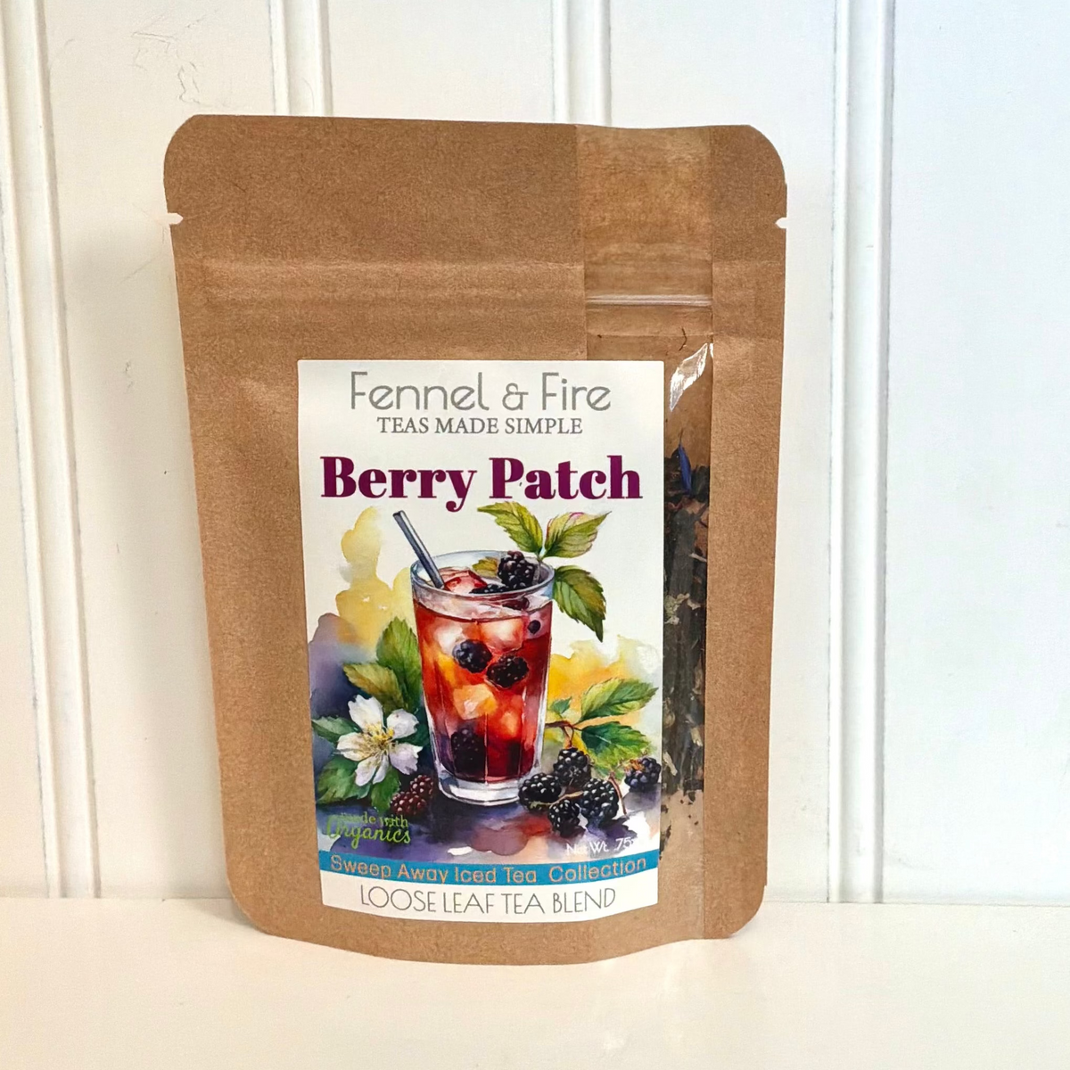 A stand-up kraft paper pouch of Fennel & Fire Berry Patch loose leaf tea blend, featuring a colorful label with a glass of berry tea and illustrations of berries and flowers, set against a white paneled background.