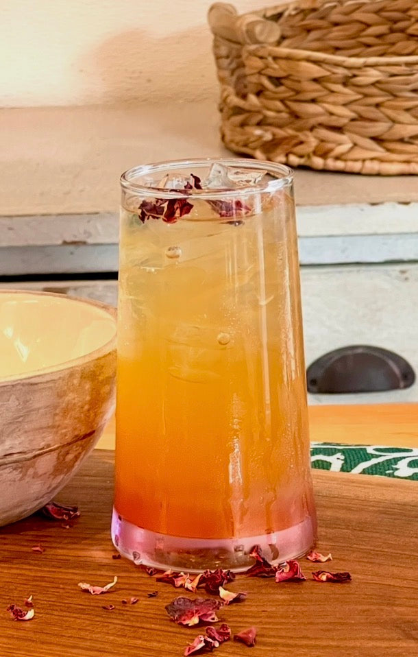 Glass of layered orange and pink drink on a wooden surface with dried hibiscus flowers.