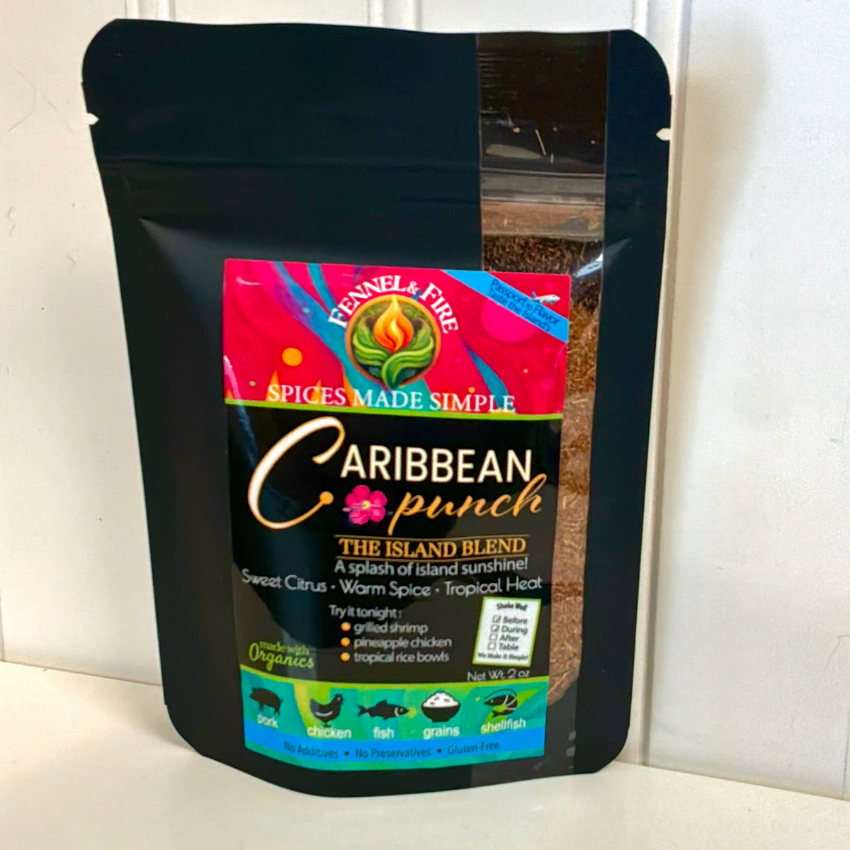 A black resealable stand-up pouch of Funnel & Fire Caribbean Punch spice blend, leaning against a white paneled wall on a white surface.