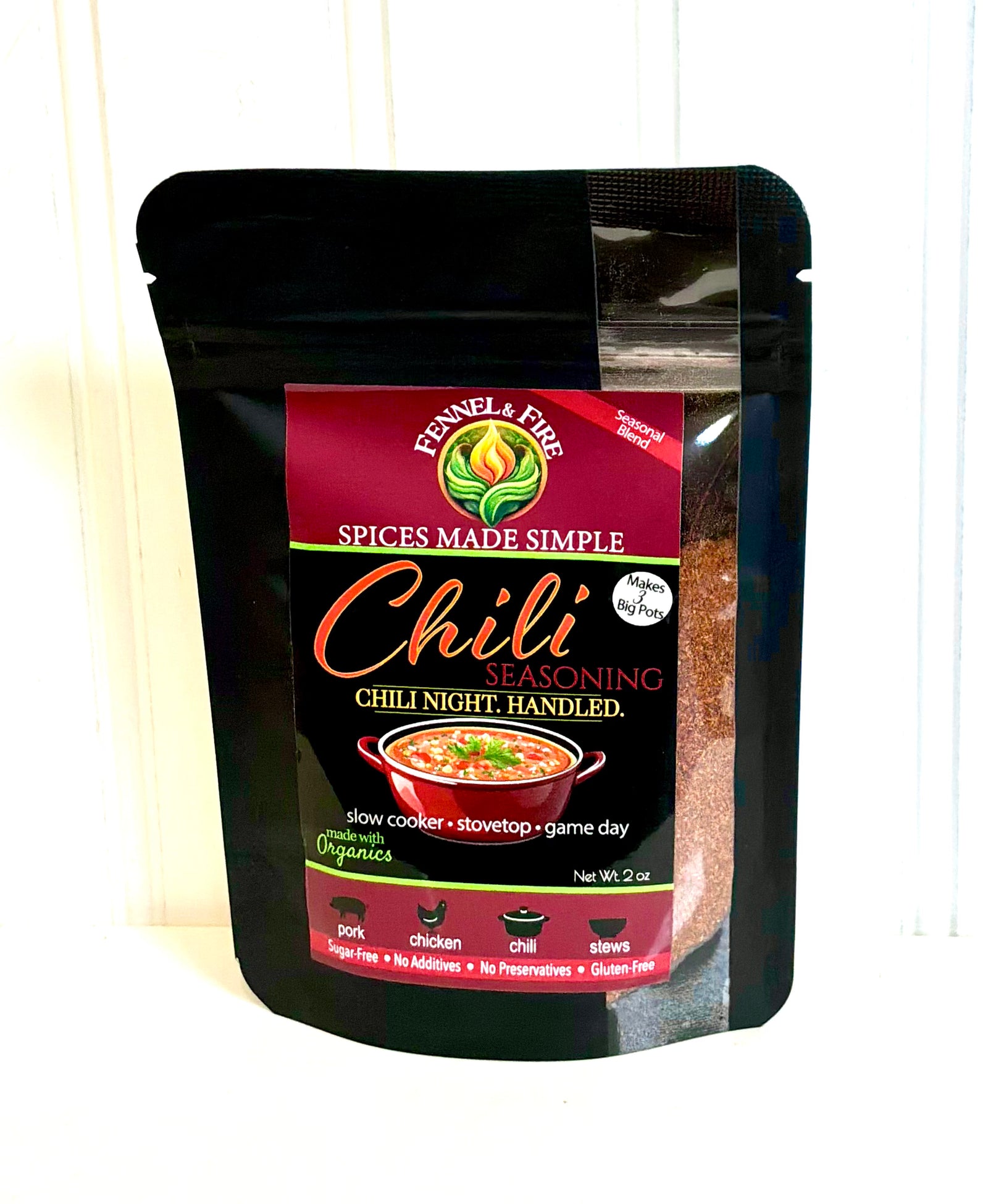 A black resealable stand-up pouch of Fennel & Fire Chili Seasoning, shown against a white paneled background. The front label is dark red and black with gold and white text, featuring a bowl of chili peppers and listing ingredients and cooking methods.