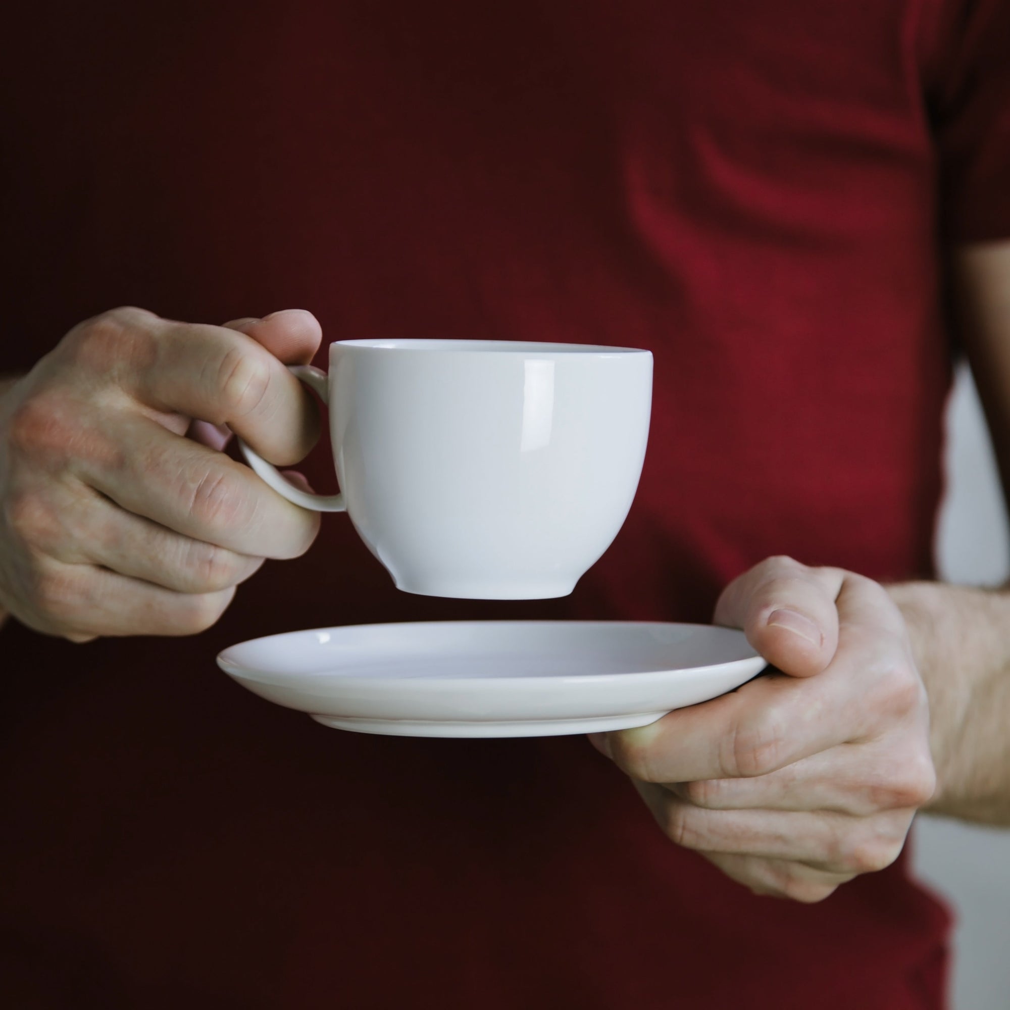 Person holding a white cup and saucer with a crimson red shirt 