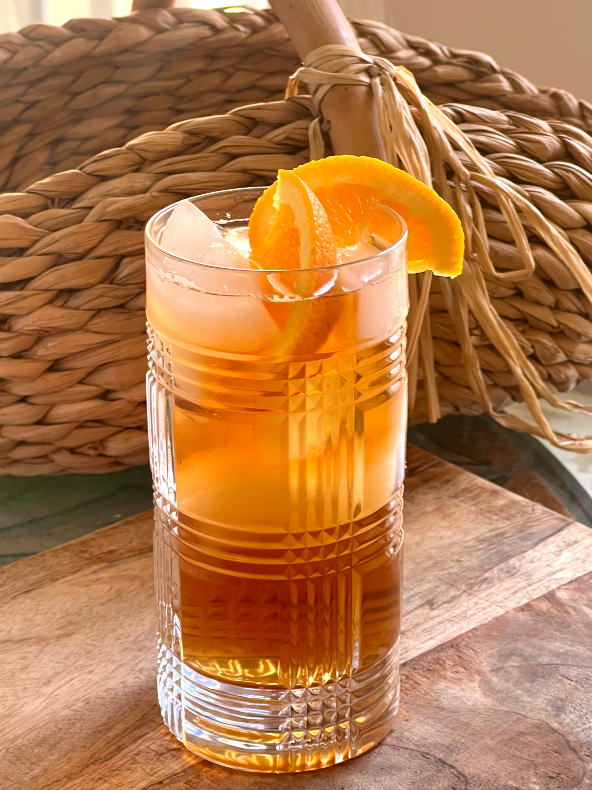 Glass of iced tea with an orange slice on a wooden surface with a woven basket in the background.