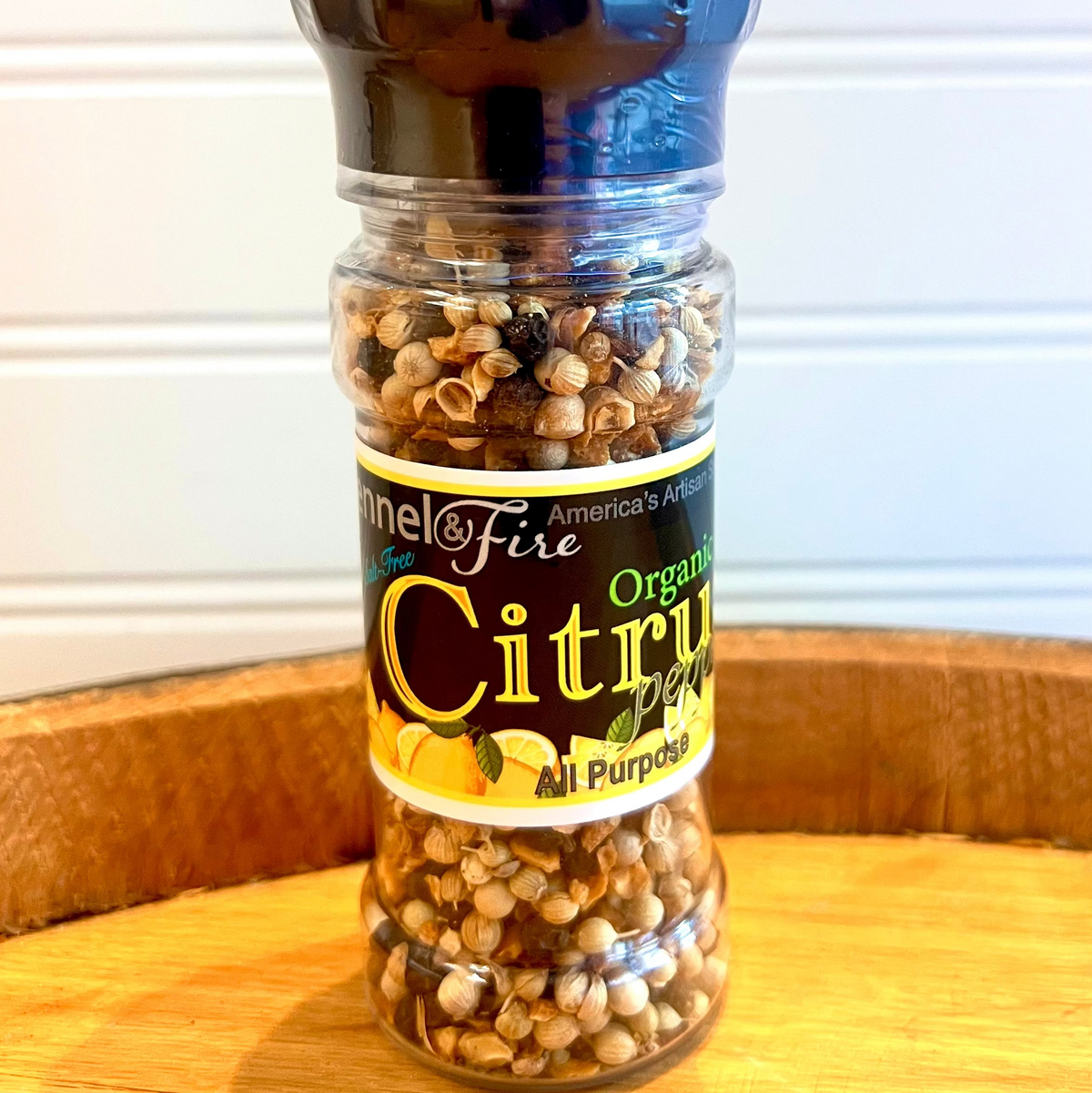 Pepper grinder labeled 'Citrus Peppercorn' on a wooden surface with a white background