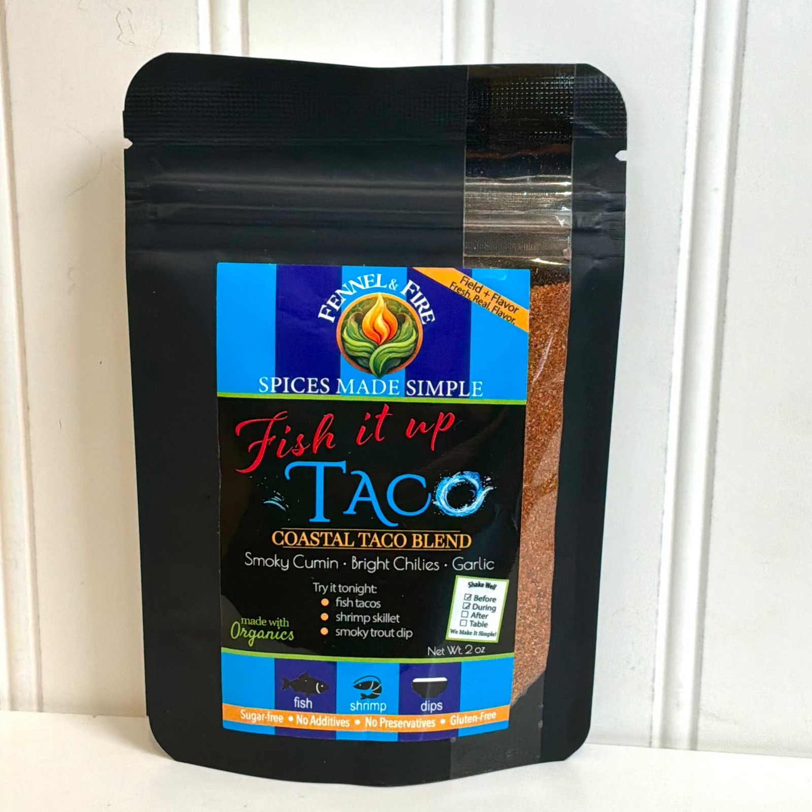 A black resealable pouch of Ennel's Fire 'Fish it up' Taco spice blend, leaning against a white paneled wall.