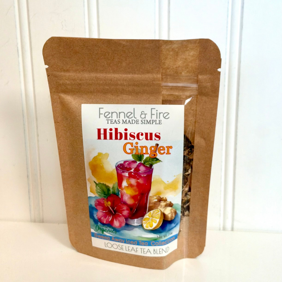 A stand-up kraft paper pouch of Fennel & Fire Hibiscus Ginger loose leaf tea blend, featuring a colorful front label with a drink, hibiscus flower, and ginger root, set against a white paneled background.