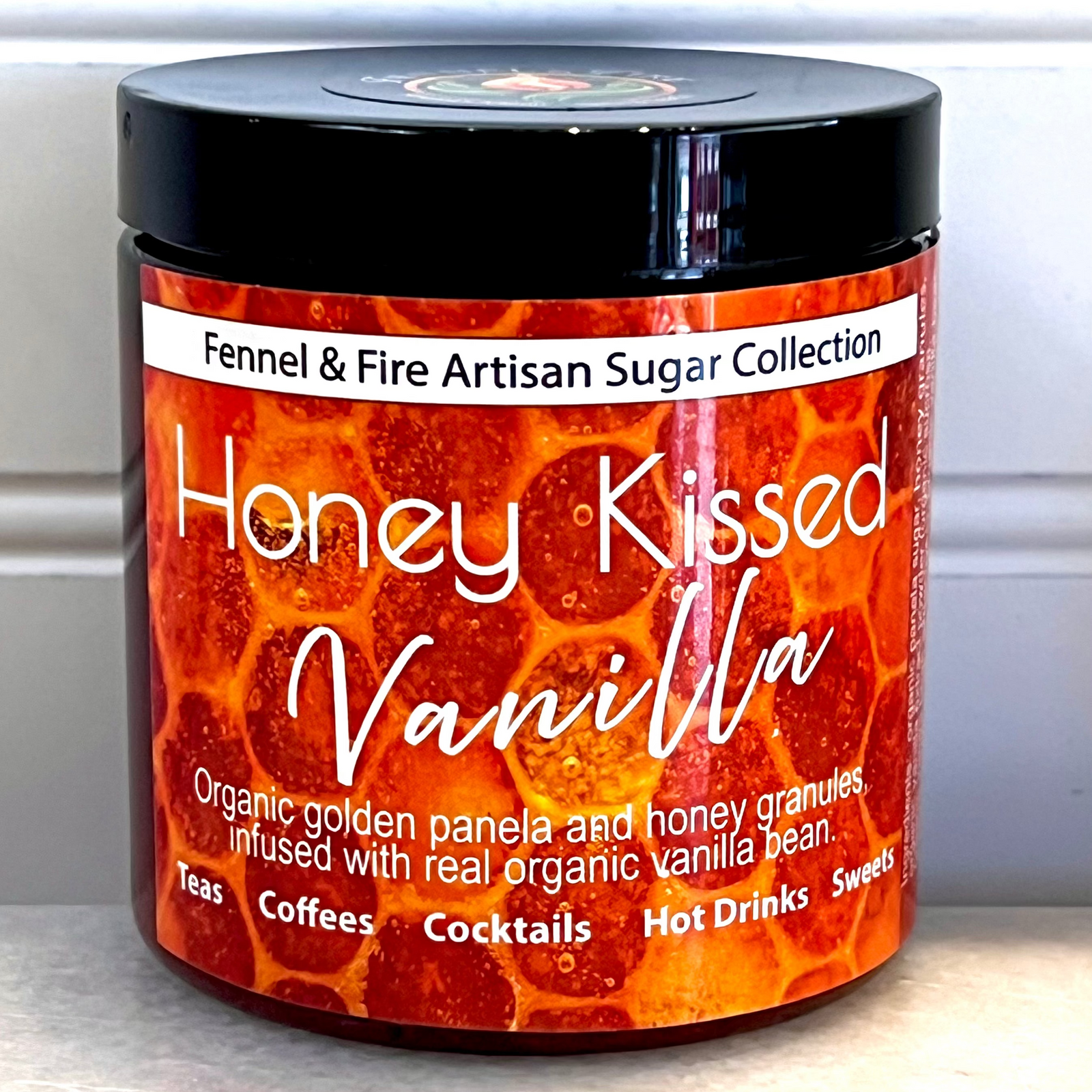 Jar of 'Honey Kissed Vanilla' sugar with a black lid on a white background