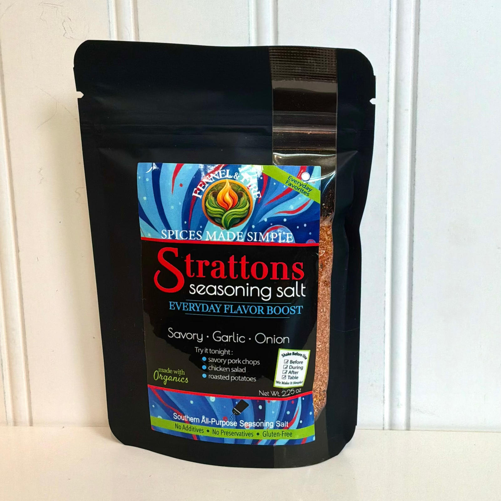 A black stand-up pouch of Strattons Seasoning Salt, Savory Garlic Onion flavor, standing on a white surface against a white paneled wall.