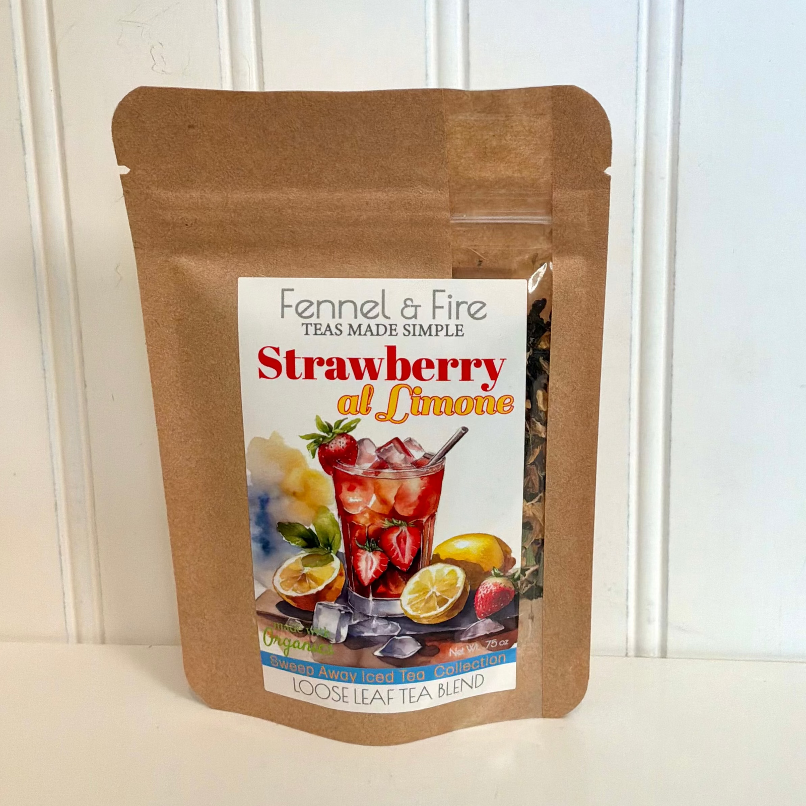 A brown kraft paper stand-up pouch of Fennel & Fire Strawberry at Lime loose leaf tea, displayed on a white surface against a white paneled wall.