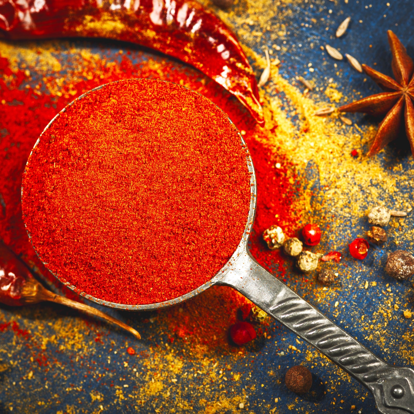 Red spice in a spoon with star anise and red peppers on a dark surface