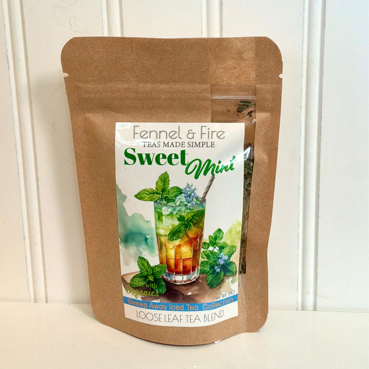 A brown kraft paper stand-up pouch of Fennel & Fire Sweet Mini loose leaf tea, featuring a colorful label with a glass of iced tea and mint leaves, set against a white paneled background.