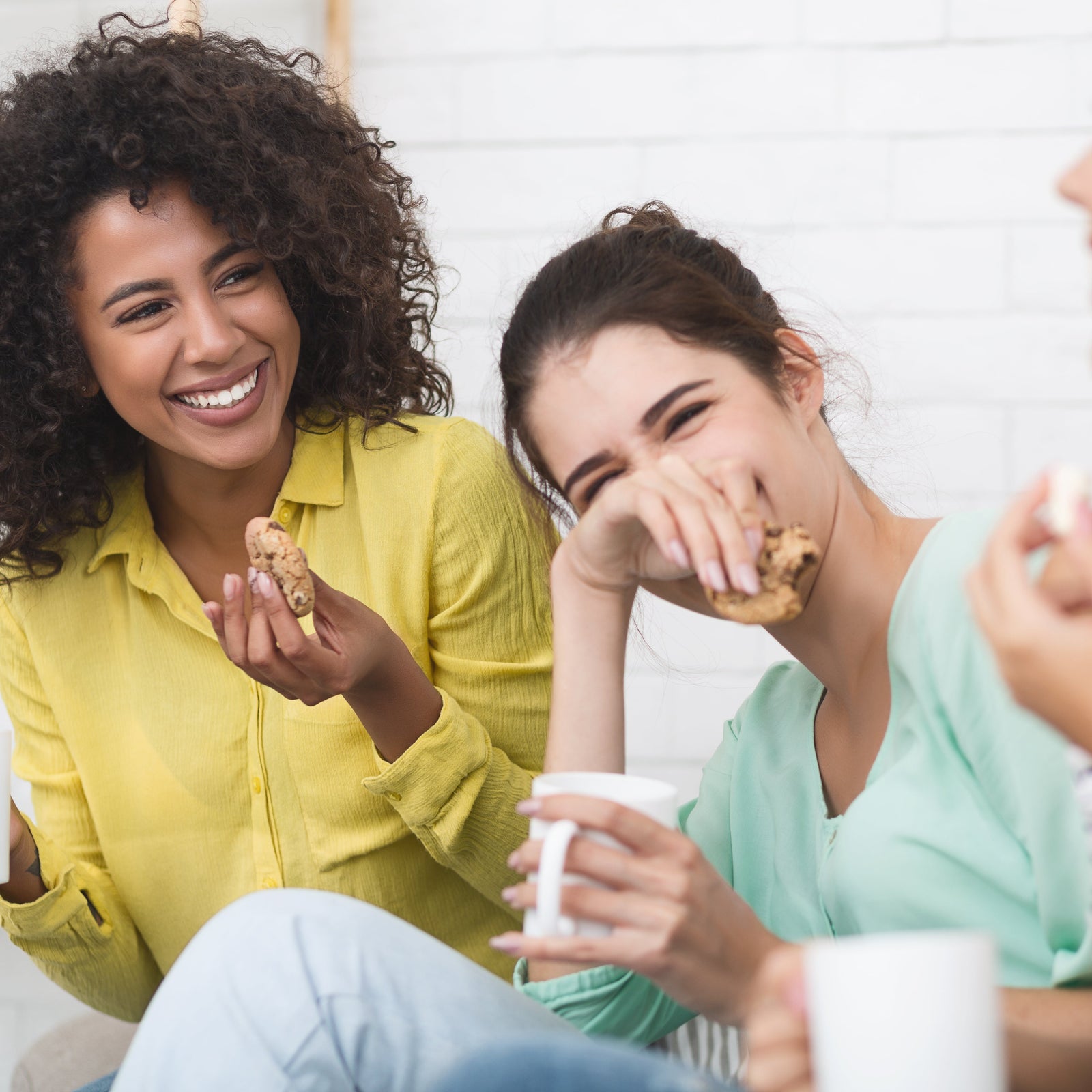 Three women sitting together, smiling and enjoying snacks and drinks.